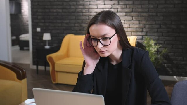 Concentrated focused woman working on laptop. Serious woman in glasses freelancer working on laptop looking at the monitor at home office. Remote work freelancer at home workplace