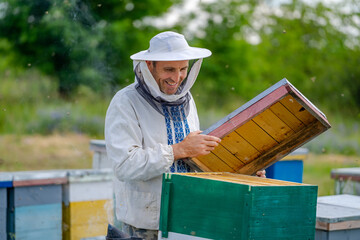 Male beekeeper over hives background. Man builds new hive Protective hat on a male`s head. Blurred background. Honey and bees concept.