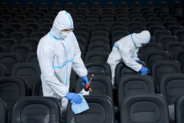 Two workers wiping chairs with disinfectants in cinema.