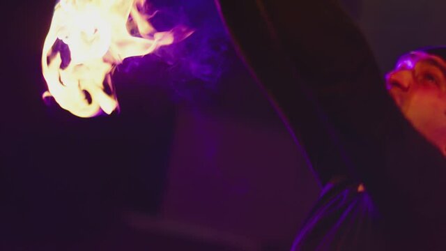 Adult man with bandanna dressed in black performing cool and dangerous fire show and doing many tricks with fire batons staff ignited from both sides each at night. Abandoned dark building. 