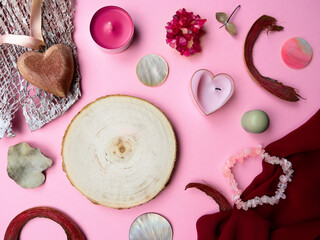 Flat lay circular tree saw cut in center,pink,pale green tone.Textured chiffon fabric,semiprecious stone bracelet,candle,dry leaves,bark pieces,wooden heart on ribbon,mother-of-pearl disks,copy space