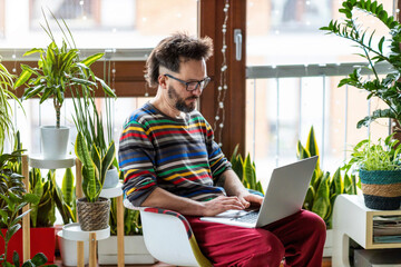 Young man working at home with laptop surrounded by houseplants