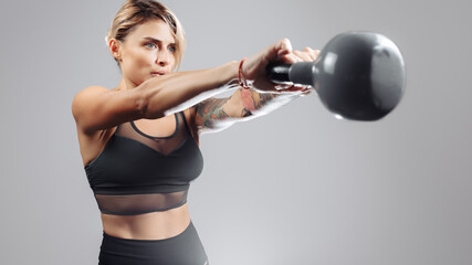 Fit young blonde woman workout in the studio with kettlebell over gray background.