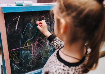 Little girl, child draws with colored chalk on a black wooden board drawing, doodle. The educational process of drawing at school.