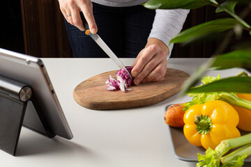 Woman cutting onion and watch virtual culinary class. Online cooking class