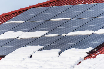 Solar photovoltaic panels PV on a snowy house roof, blue sky with copy space. - 411006061