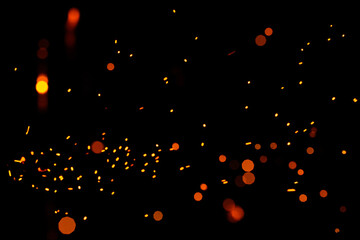 Particles of burning embers fly and glow isolated in the night sky. Bright yellow sparks on a black background, yellow bright round bokeh.