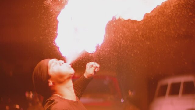 Adult man with bandanna dressed in black performing cool and dangerous fire show,  spraying kerosene on  torch and erupting flame. Circus performer emits fire out of his mouth. Slow motion shot. 