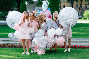 Six girls are having fun at a party in the park. They're wearing pink dresses and a bunch of pink balloons