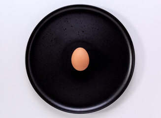 A single brown egg in the centre of a black plate on a white background