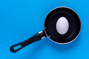 A small frying pan with a white egg on a blue background