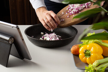 Woman cutting onion and watch virtual culinary class. Online cooking class