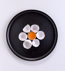 An egg yolk surrounded by empty eggshells on a black plate