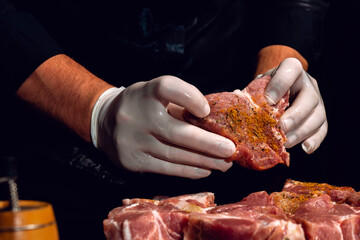 Marinating pork neck skewers, adding salt, curry and basil to the meat, pieces of meat on a wooden board.