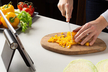 Woman cutting pepper and watch virtual culinary class. Online cooking class