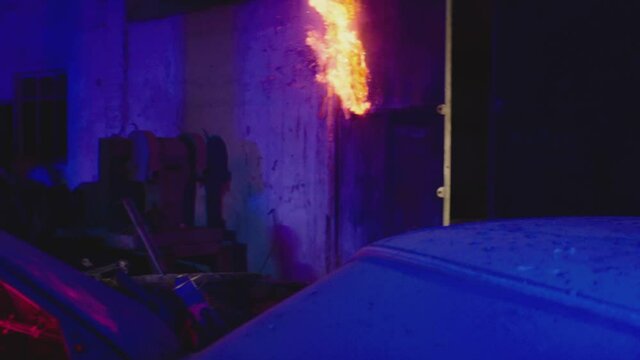 Young male protester covered his face with black bandanna mask   throwing bottle of Molotov cocktail in concrete wall on abandoned building at night. House burning down on fire. Slow motion shot