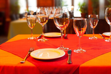 Served table with plate fork knife and beautiful wine glasses on red and orange tablecloths. Soft focus, shallow depth of field background.