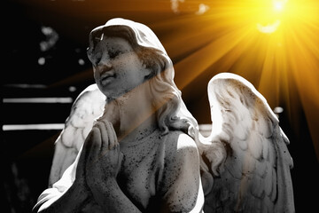 Praying angel against dark background. Ancient statue.