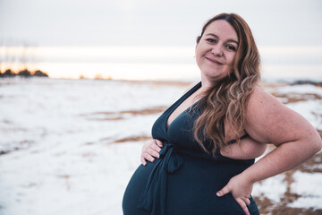 Beautiful pregnant brunette model wearing flowing dress surrounded by winter landscape