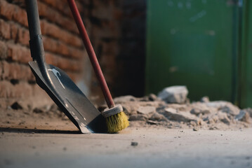 Shovel and broom on the dusty construction site floor background.