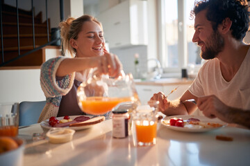 A happy young couple enjoying fresh orange juice for a breakfast. Relationship, love, together,...