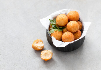 Deep-fried potato and cheese croquettes with parsley in a ceramic bowl on a light gray background...