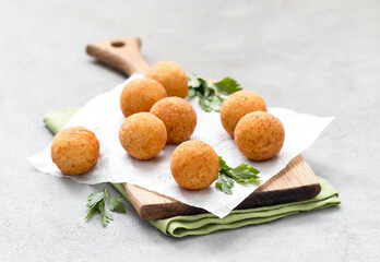 Potato balls croquettes with parsley on a wooden board on a light gray background