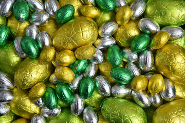 Large & small yellow, gold, green, lime green and silver spring colours of foil wrapped chocolate easter eggs, against a black background.