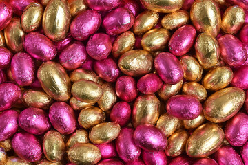 Large & small pink and gold foil wrapped chocolate easter eggs, against a peach orange background.
