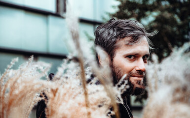 Artistic photo portrait confident smiling handsome middle-aged Caucasian man portraited in the city, with white skin, grey and black hair having a friendly look on his face, wearing a blue jacket.