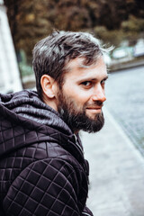 Artistic photo portrait confident smiling handsome middle-aged Caucasian man portraited in the city, with white skin, grey and black hair having a friendly look on his face, wearing a blue jacket.