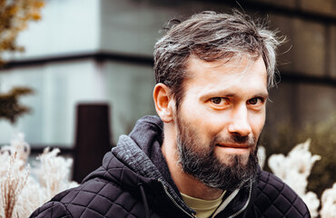 Artistic photo portrait confident smiling handsome middle-aged Caucasian man portraited in the city, with white skin, grey and black hair having a friendly look on his face, wearing a blue jacket.