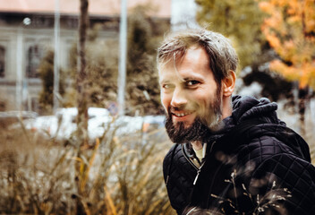 Smiling handsome young or a middle-aged Caucasian man portraited in the city, with white skin, grey and black hair having a friendly and confident look on his face. Background with fall moody colours 