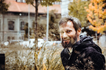 Smiling handsome young or a middle-aged Caucasian man portraited in the city, with white skin, grey and black hair having a friendly and confident look on his face. Background with fall moody colours 