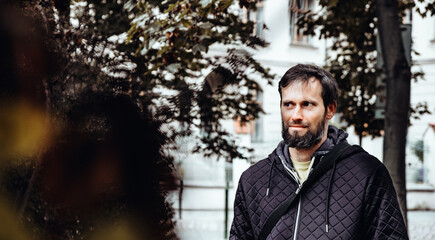 Artistic photo portrait confident smiling handsome middle-aged Caucasian man portraited in the city, with white skin, grey and black hair having a friendly look on his face, wearing a blue jacket.