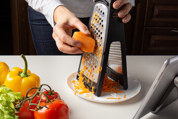 Woman grating carrots and watch virtual culinary class. Online cooking class