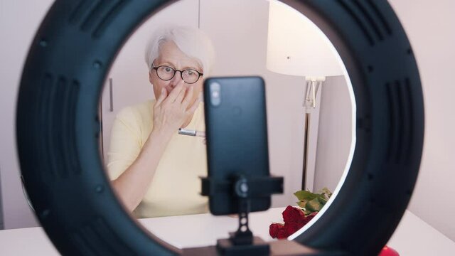 Elderly woman having a video call while applying make up and getting ready for valentines day date. High quality 4k footage