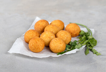Deep-fried potato balls with parsley on paper on a light gray background