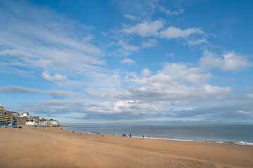 A winter beach in Ramsgate on a blue sky day with fluffy white clouds. A few unrecognisable people are walking on the beach.