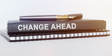 On the table are a notebook, a pen and a book. The book says - CHANGE AHEAD