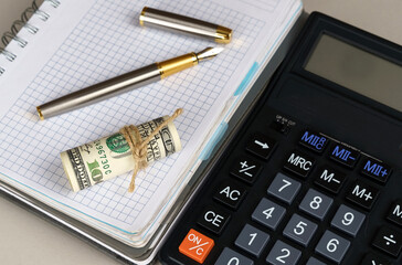 On the table is a notebook with a pen and dollars, next to a calculator