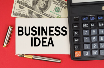 On a red background, among the money, a calculator and a pen lies a sign with the text - BUSINESS IDEA