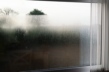 Condensation on the outside of double glazed window glass at sunrise. The window has vertical slat...