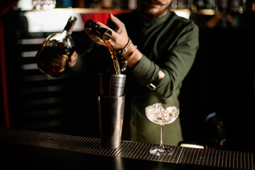 view of jigger in hand of bartender from which he pours drink into shaker cup