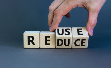 Reuse or reduce symbol. Businessman turns wooden cubes and changes the words reduce to reuse. Beautiful grey background, copy space. Business, ecological and reduce or reuse concept.
