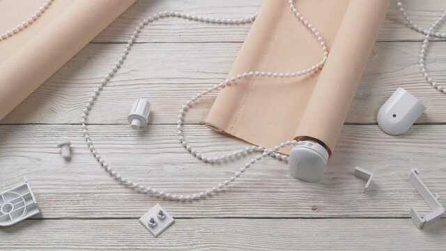 The two beige roller blinds and spare parts on a white wooden table. Preparation for the installation of roller blinds.