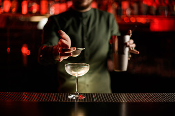 empty glass stands on the bar counter and hand of bartender holds sieve over it