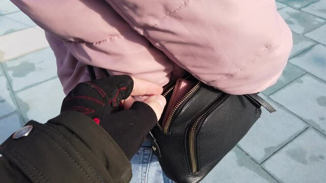 Thief steals a purse from a girl's handbag outdoor. Street theft of a wallet from a woman's purse.