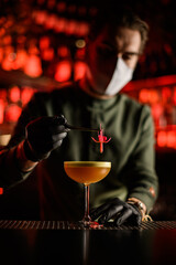 male bartender holds flower with tweezers and decorates glass of cocktail with it