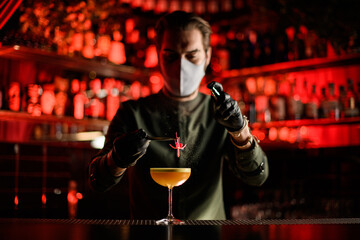 view of bartender who holds flower with tweezers over glass of cocktail and sprinkles on it